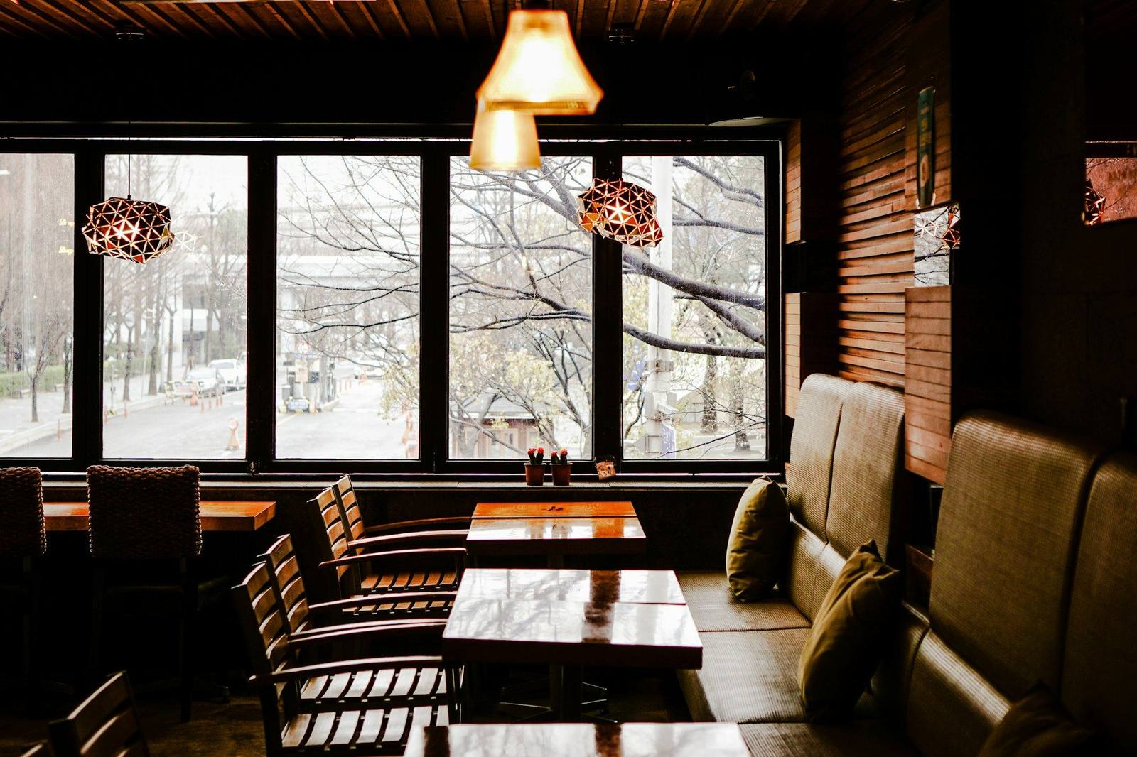 Salón de café con mesas de madera, lámparas colgantes y ventanales a la calle